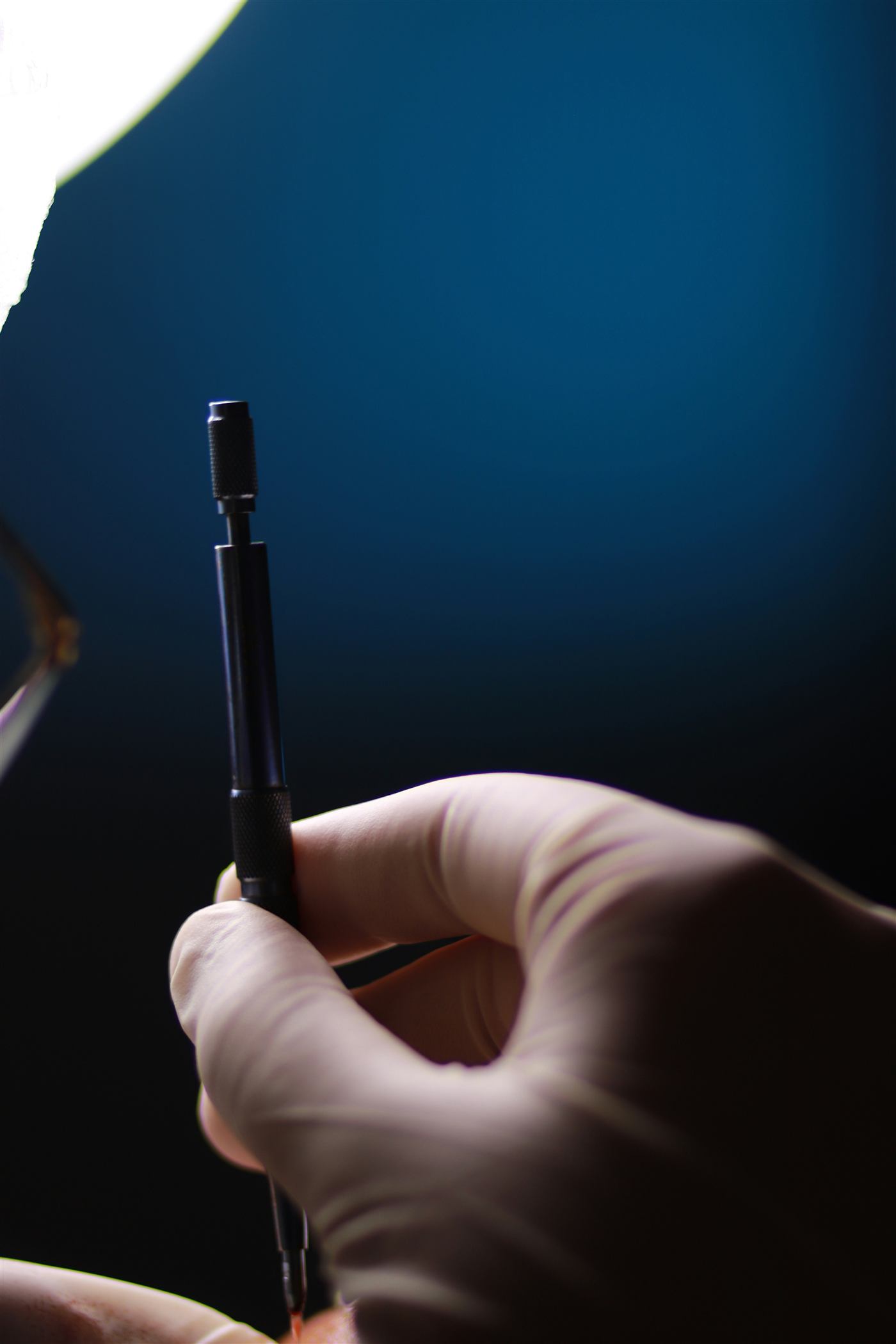 Gloved hand holding a surgical instrument against deep blue theatre light